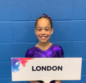 A young student, competing in a gymnastics competition holding a sign saying London